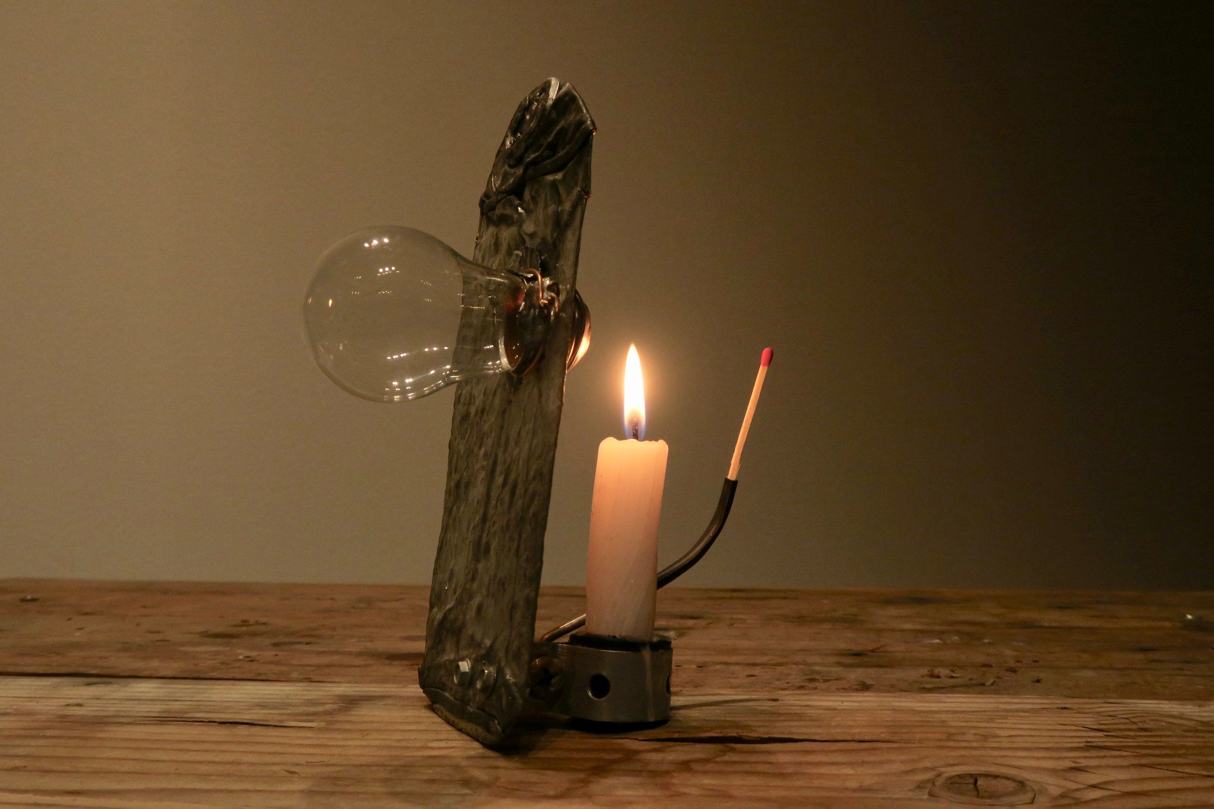 A sculpture of driftwood, a glass bulb, a lit candle and a match on a wooden table
