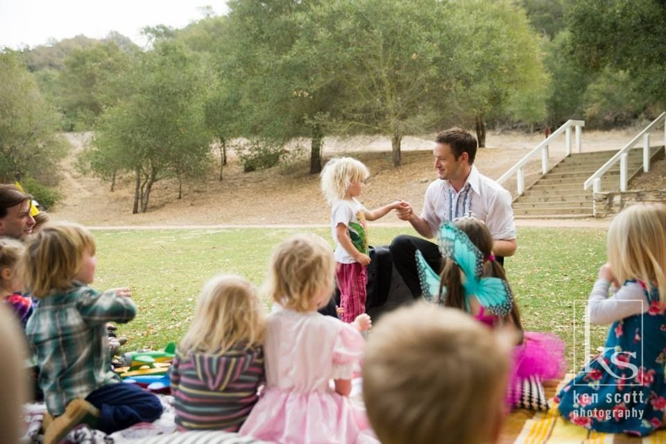 Magic Mark performs for a circle of young children sitting on the grass