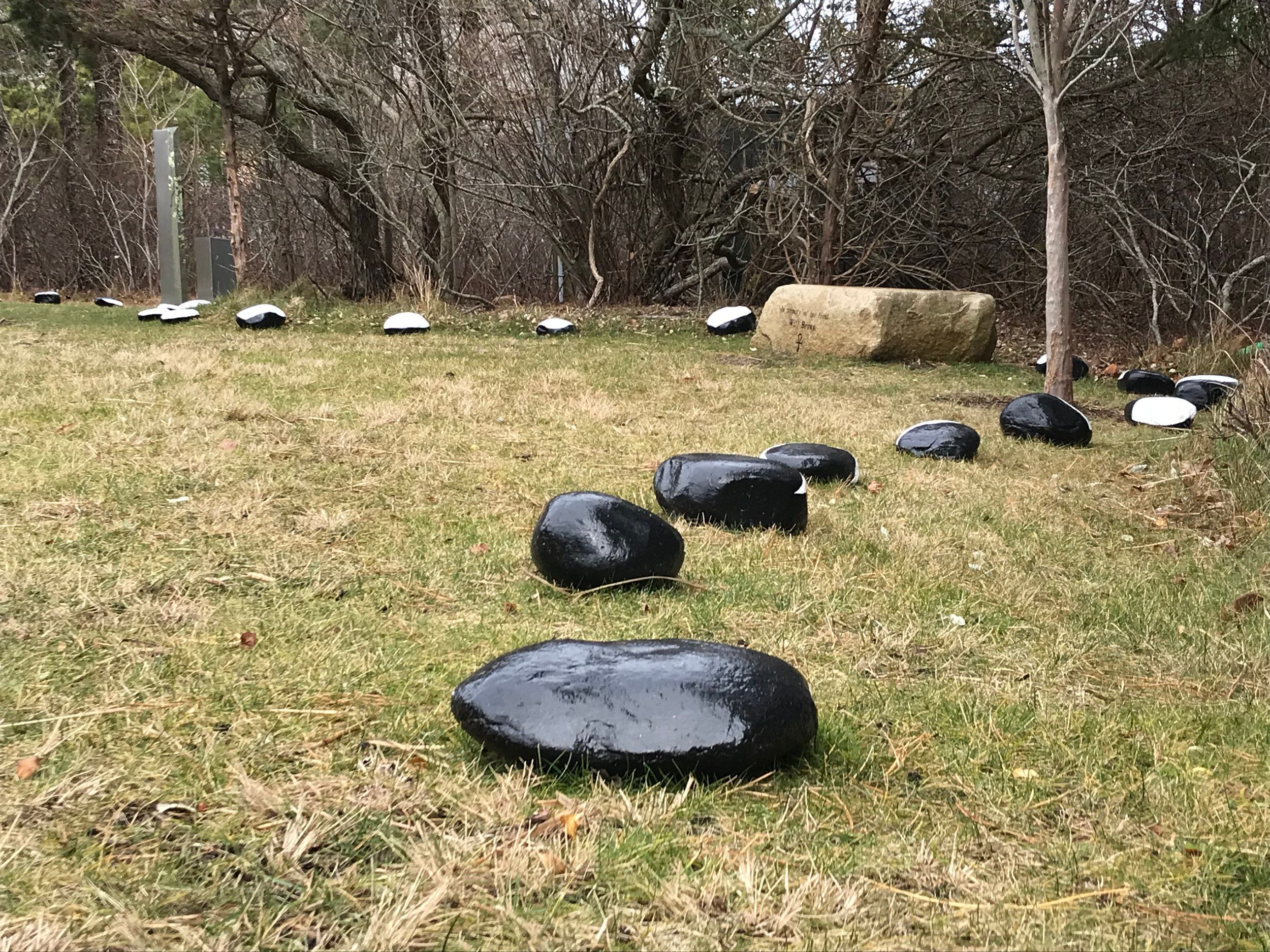 A winding line of black and white painted stones across a meadow, each one a phase of the moon