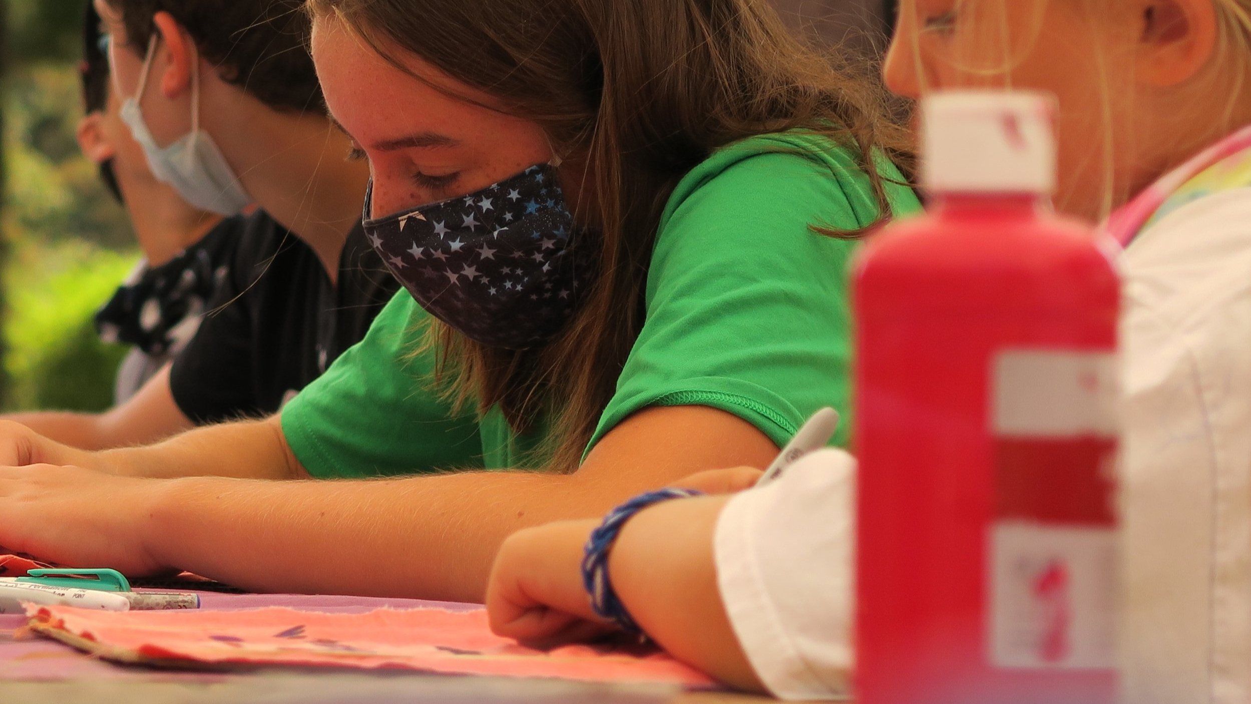 Students in masks bent over their flags, painting at a long table
